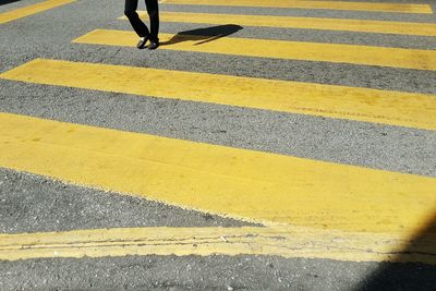 Low section of person walking on zebra crossing during sunny day