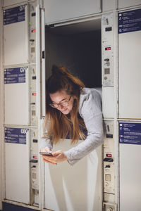 Young woman using phone in locker