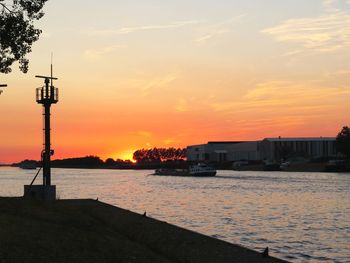 Silhouette buildings by river against sky during sunset