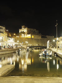 Boats moored on river by illuminated buildings in city at night