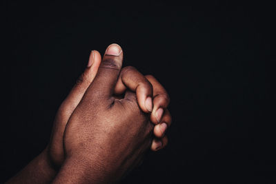 Close-up of hands clasped over black background