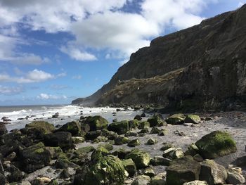 Rocky mountain at beach against cloudy sky