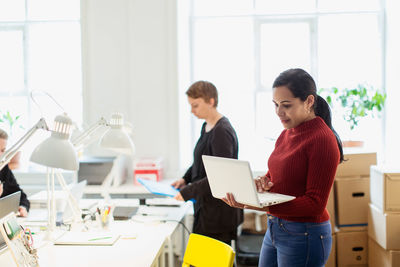 Confident businesswoman using laptop while standing at creative office