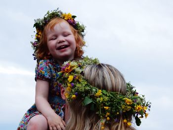 Portrait of happy girl with flowers against sky