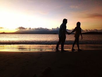 Silhouette friends on beach against sky during sunset