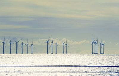 Wind turbines by sea against sky