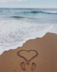 Heart shape on sand at beach against sky