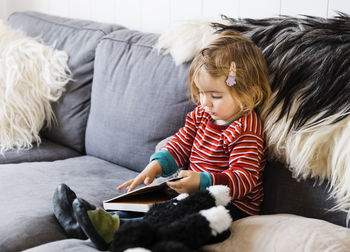 Cute girl with book sitting on sofa at home