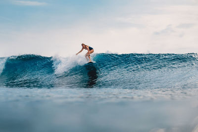 Side view of woman surfing in sea against sky