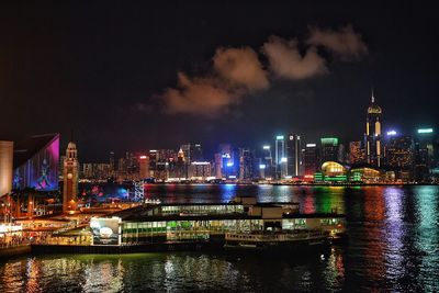 Illuminated cityscape at victoria harbour against sky at night