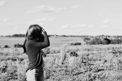 Rear view of woman photographing on field against sky