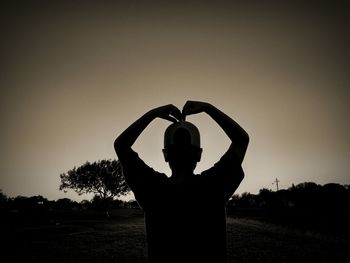 Silhouette woman with arms raised standing on field against clear sky