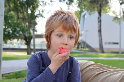 A blond boy is eating a watermelon and the juice is flowing down his arm.  