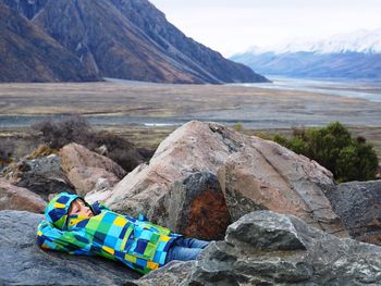 Boy lying on rocks against mount cook