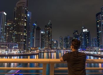 Rear view of man looking at illuminated modern buildings in city at night