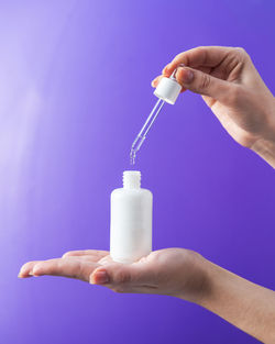 Cropped hand holding syringe against blue background