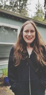 Portrait of smiling woman standing against house in yard