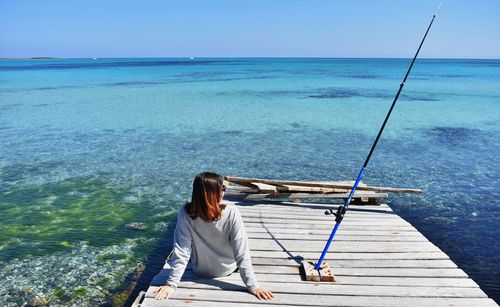 Rear view of woman sitting on sea against sky