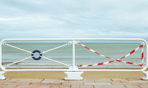 Metallic railing by sea against sky