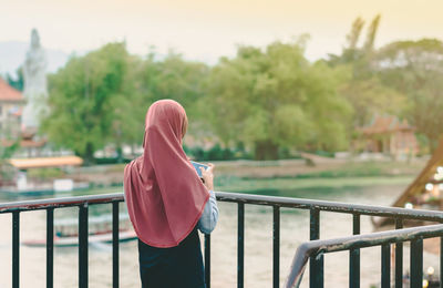 Rear view of woman standing by railing against trees