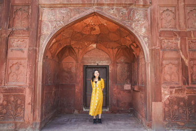 Ethnic young barefoot woman in traditional clothes walking and looking at camera against aged arch door in the red fort in new delhi, india