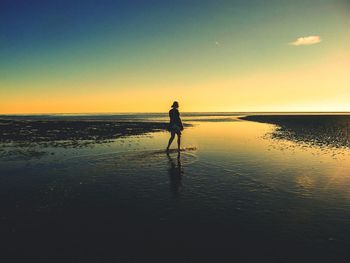 Rear view of woman walking at beach during sunset