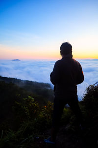 Rear view of silhouette man standing on mountain against sky