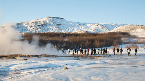 People standing by hot spring against snowcapped mountain