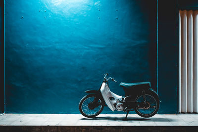Motor scooter parked on sidewalk against blue wall at night