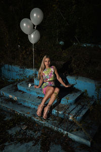 High angle portrait of young woman with balloons sitting outdoors at night