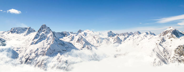 Panorama of mountains above the clouds under a clear sky on a sunny day