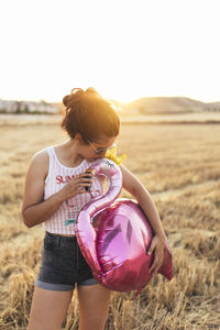 Woman kissing flamingo balloon on field at sunset