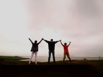 Rear view of people with arms raised standing on land against sky