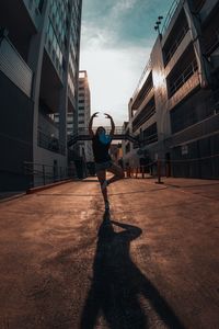 Full length of woman dancing amidst building against sky