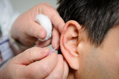 Cropped hands of doctor stitching patient ear at hospital