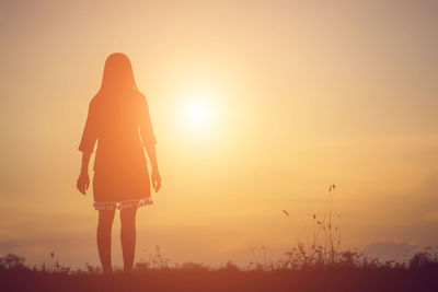 Rear view of silhouette woman standing on field during sunset