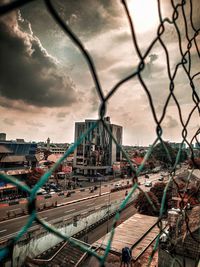 Cityscape seen through chainlink fence against sky