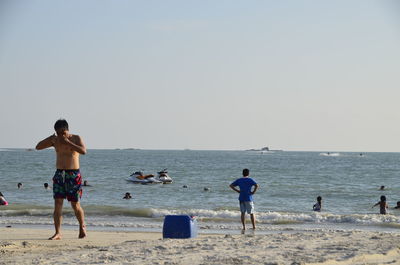 Full length of shirtless man walking at beach against clear sky