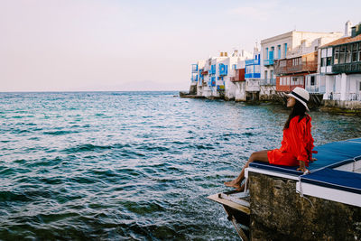 Rear view of man sitting on sea against sky