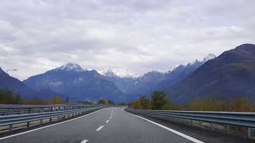 Empty road leading towards mountains against sky