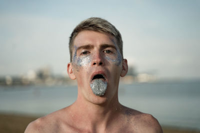 Portrait of young man with glitter in mouth against sea