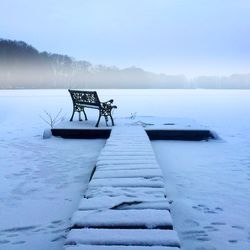 Pier on frozen lake against sky during winter