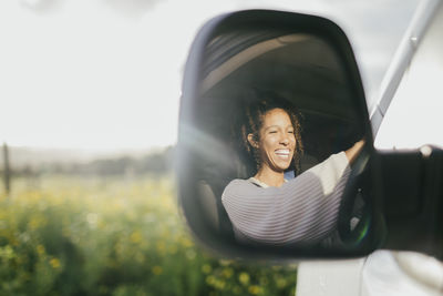 Cheerful young woman driving van seen through side-view mirror