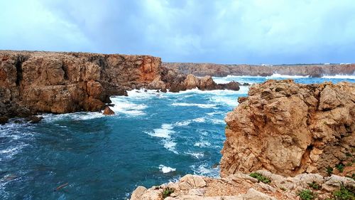 Rock formations in sea against cloudy sky