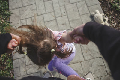 Cropped image of father holding daughter's hands while playing on footpath in yard