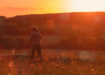 Rear view of man standing on field against sky during sunset