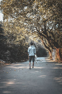 Rear view of young man holding skateboard while walking on road