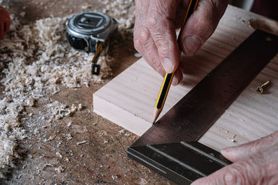 Cropped hands of carpenter measuring wooden plank in workshop