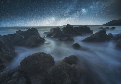 Scenic view of rocks at sea against sky at night