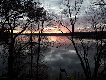 Silhouette bare trees by lake against sky during sunset